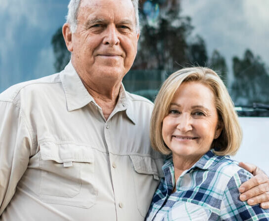 Ein älterer Mann hält eine ältere Frau seitlich im Arm, beide lächeln