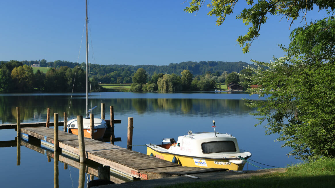 Ein Bootssteg am Ufer des Waginger Sees, an dem zwei Boote angebunden sind