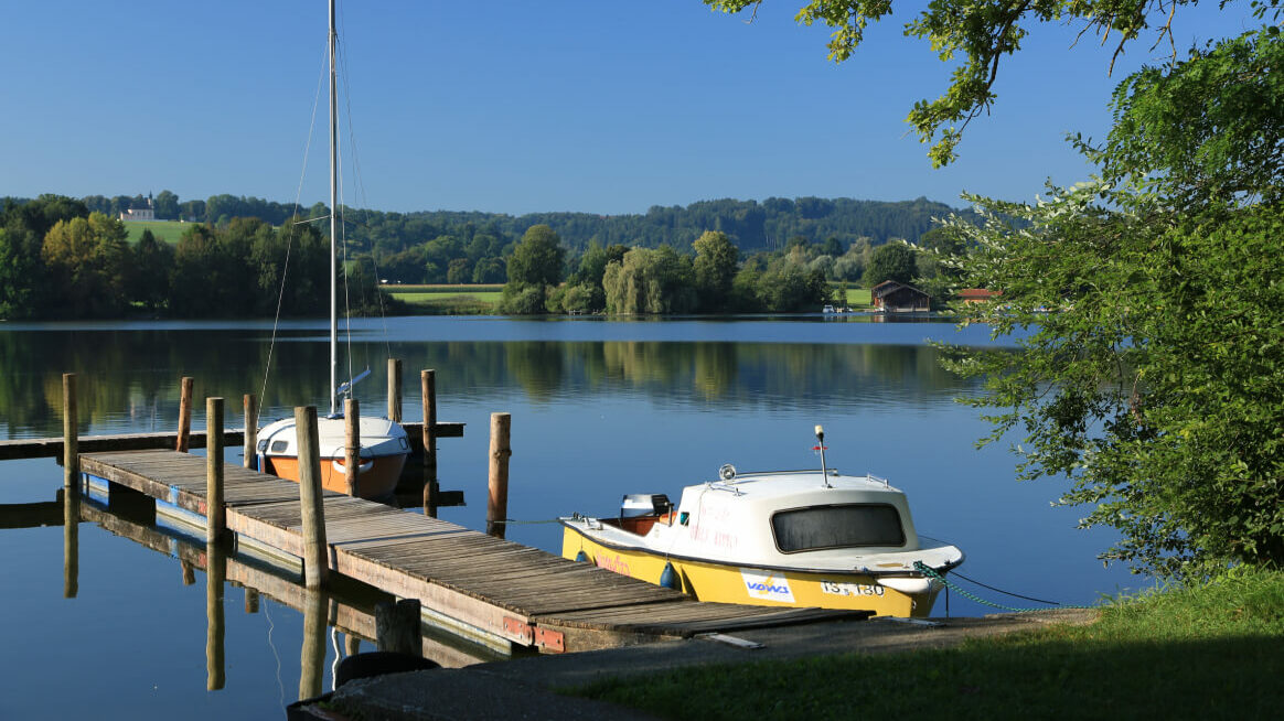Ein Bootssteg am Ufer des Waginger Sees, an dem zwei Boote angebunden sind