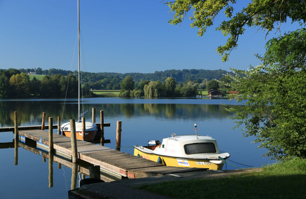 Ein Bootssteg am Ufer des Waginger Sees, an dem zwei Boote angebunden sind