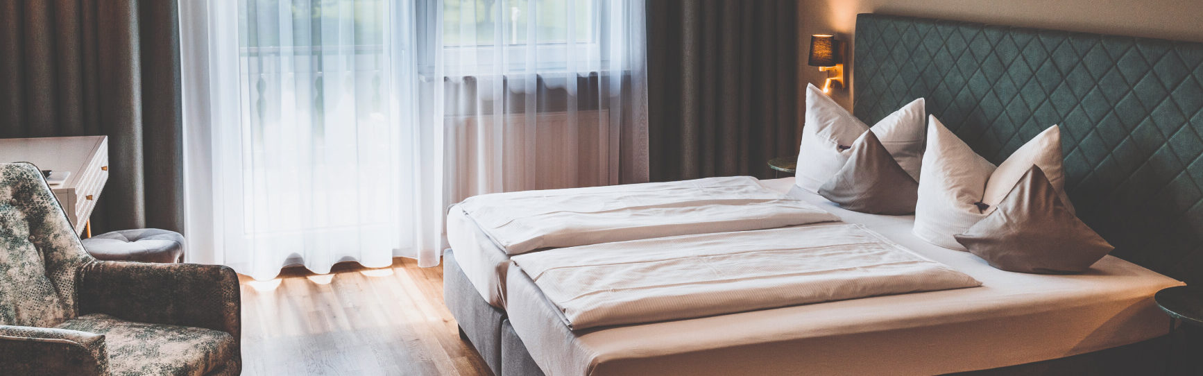 Innenansicht eines frisch hergerichteten Zimmers mit einem Doppelbett und einem Tisch und Sessel