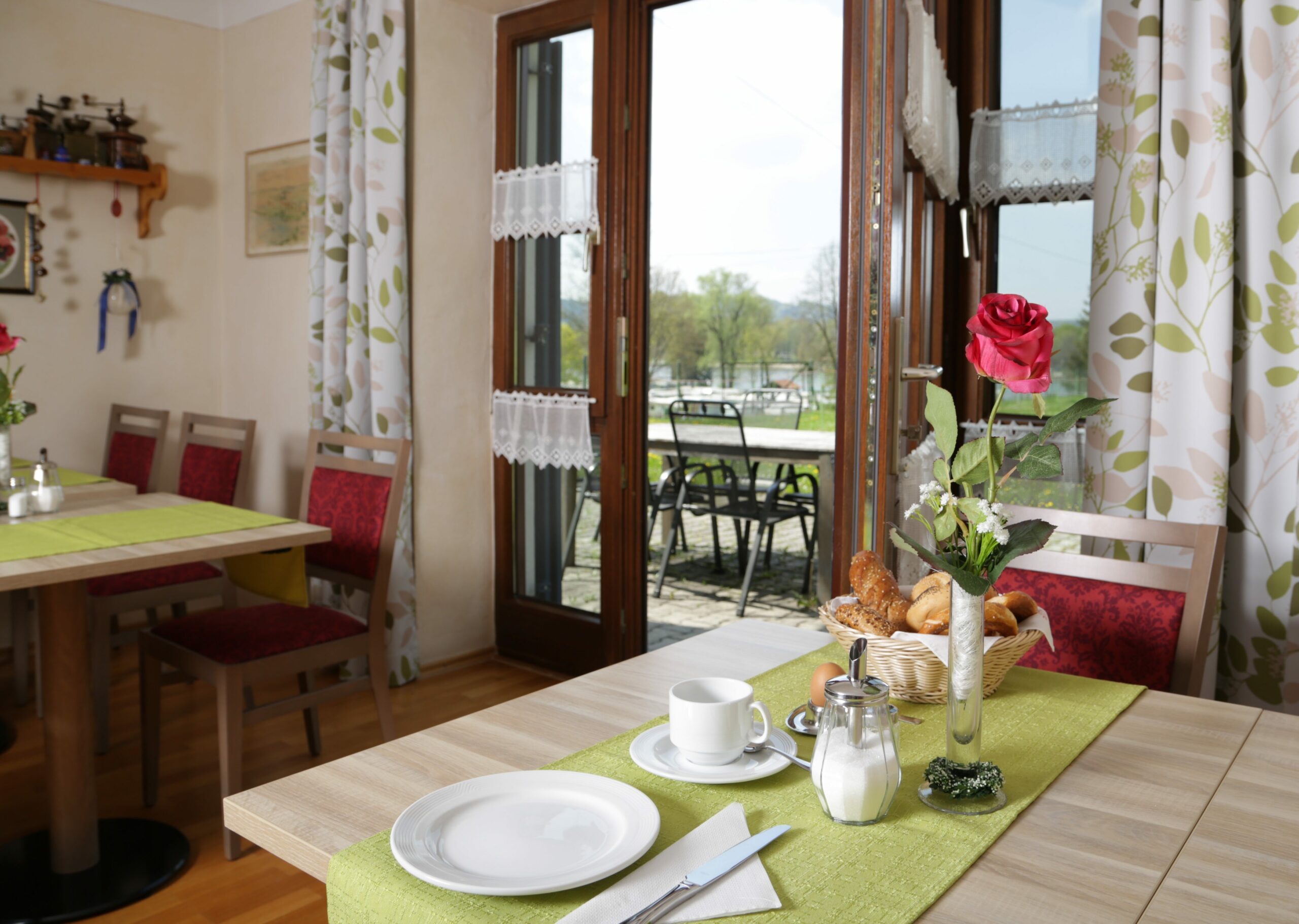 Ein übbig gedeckter Frühstückstisch mit einem Frühstücksei und Brot. Im Hintergrund ist die große Terasse mit weiteren Tischen zu sehen.