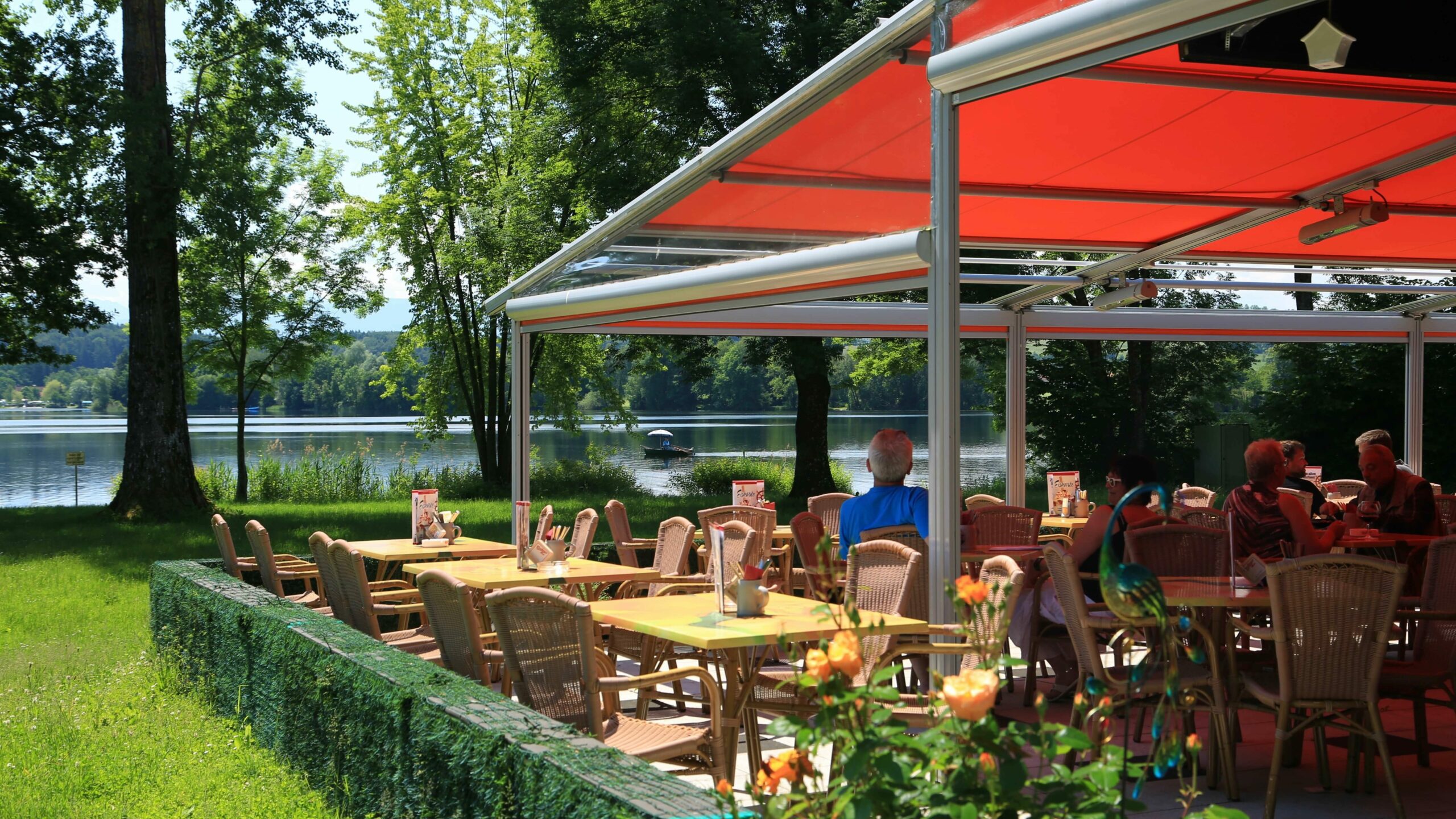 Außenansicht der mit einem Schirm überdachten Terrasse des Restaurants zum alten Fährhaus vor dem See.