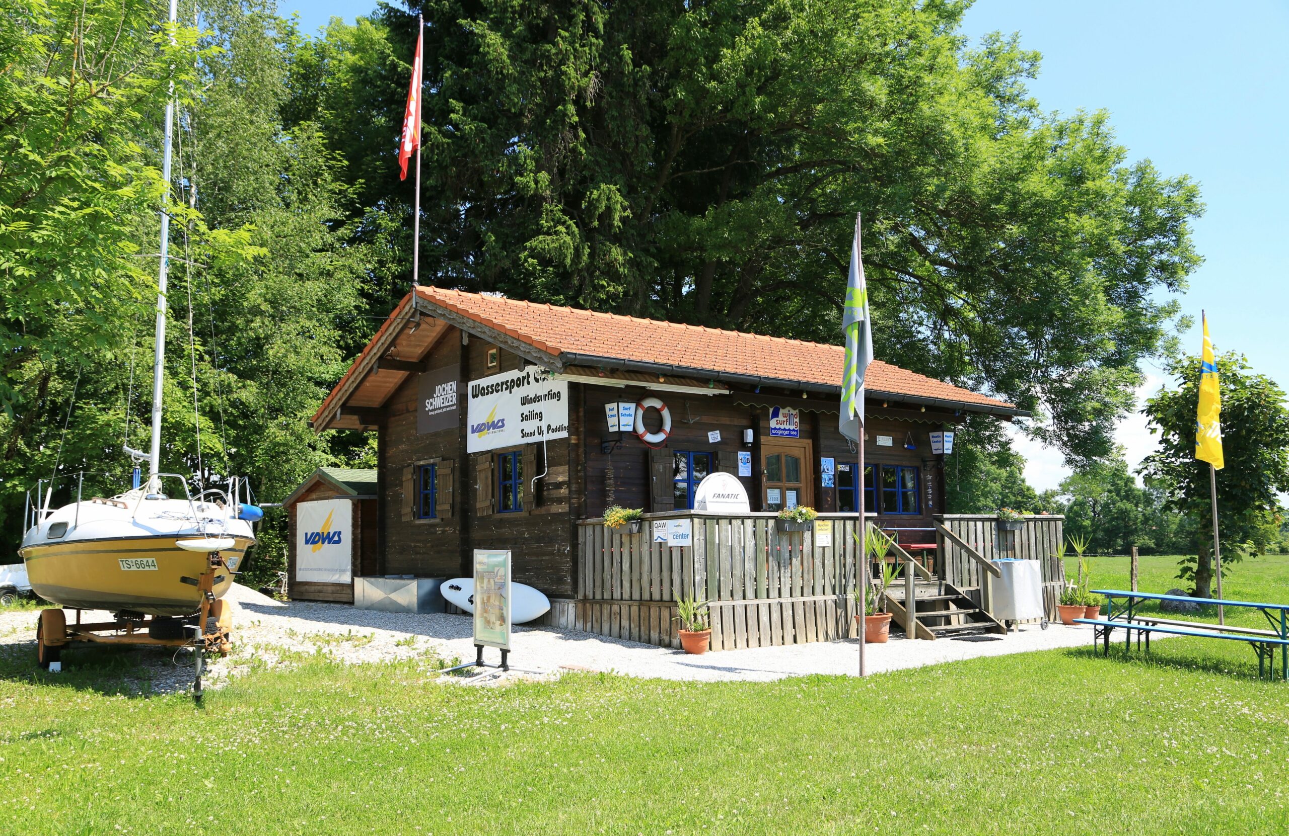 Außenansicht des Wassersport Centers. Vor dem Haus steht ein Boot und ein Surfbrett, sowie eine Biertisch