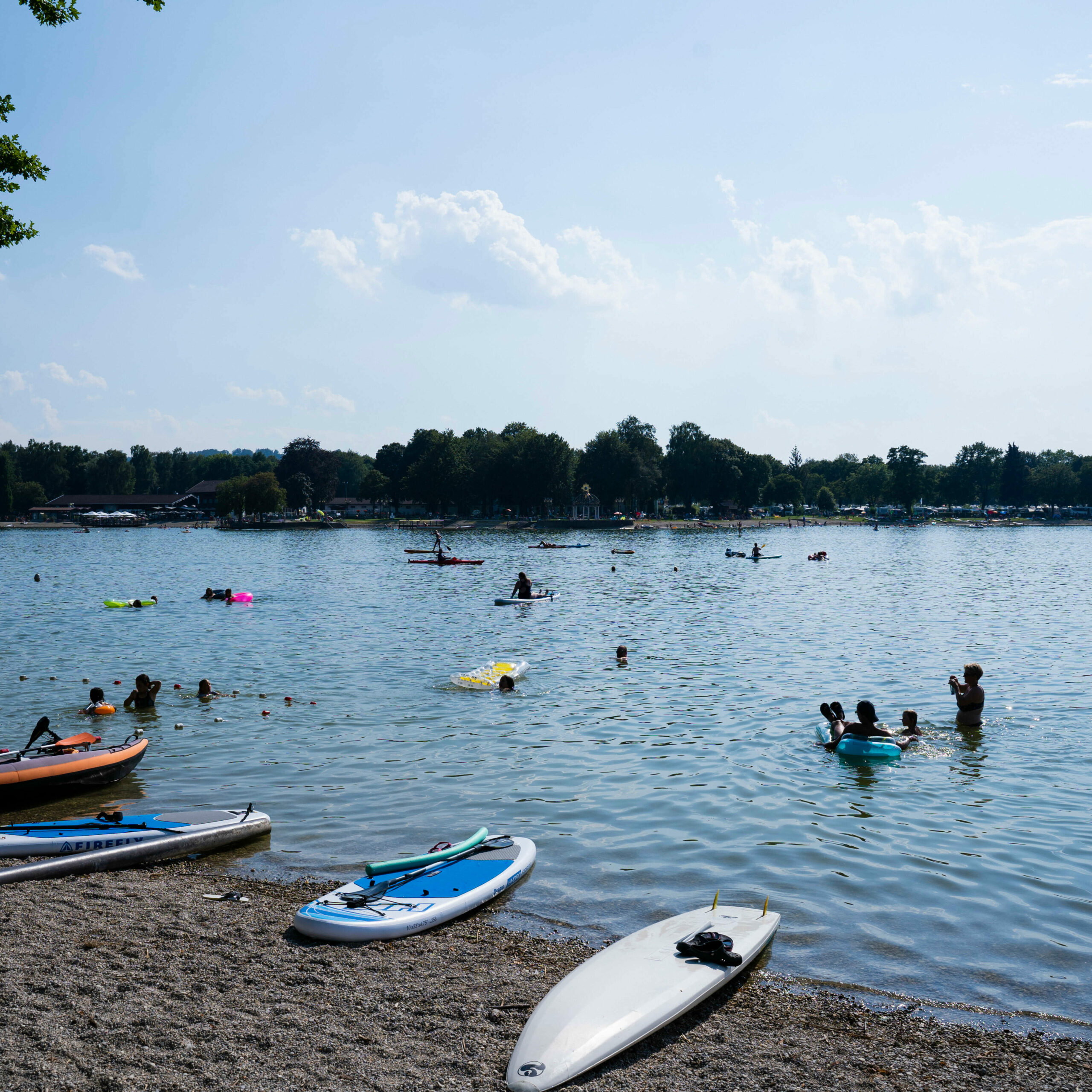 mehrere Personen, die am Kiesstrand des Waginger Sees baden
