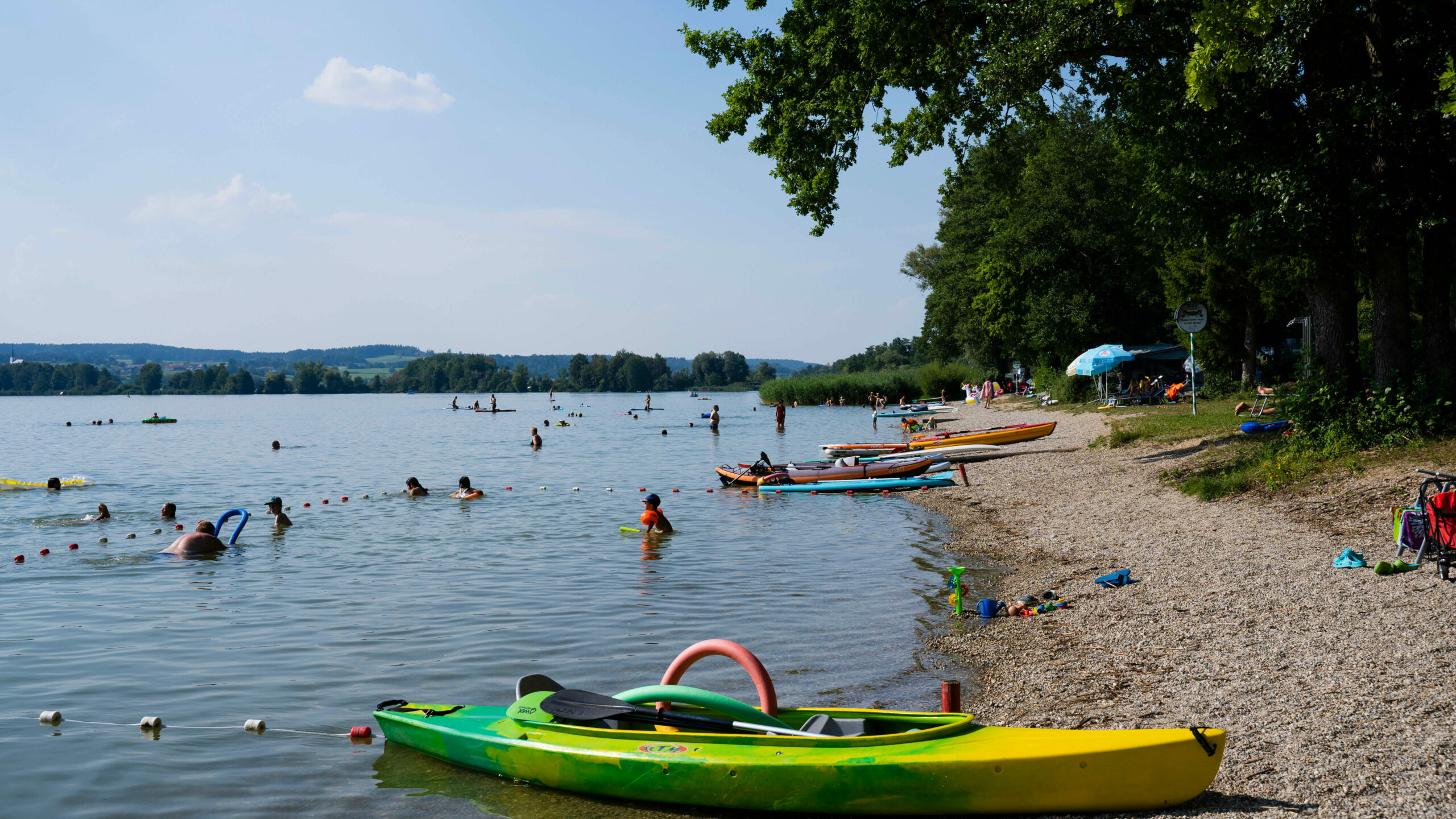 mehrere Personen, die am Kiesstrand des Waginger Sees baden