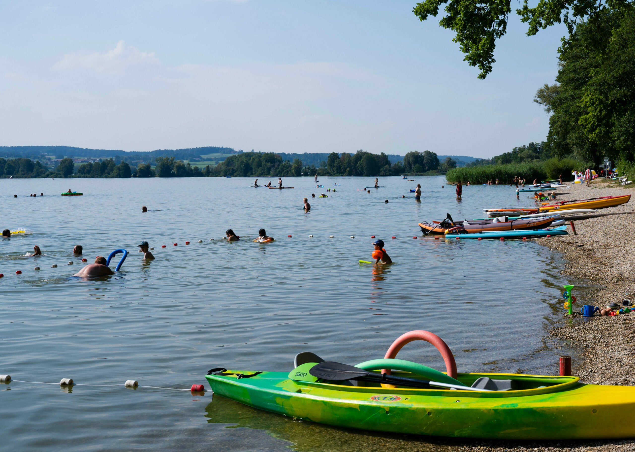 mehrere Personen, die am Kiesstrand des Waginger Sees baden