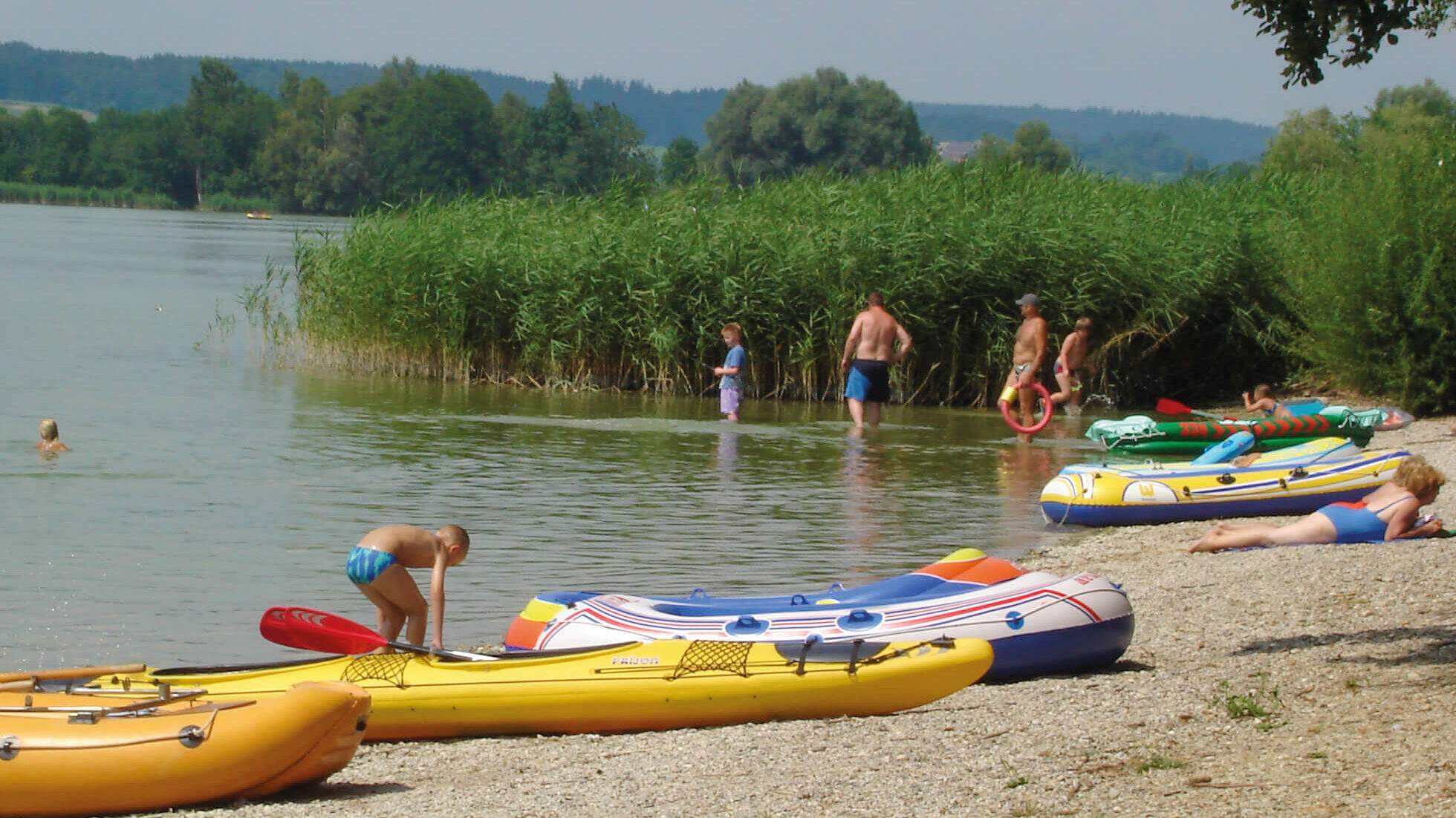 Einige badende Leute und kleine Boote am Kiesstrand des Waginger Sees