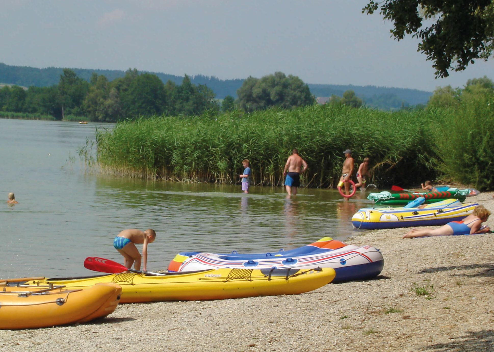 Einige badende Leute und kleine Boote am Kiesstrand des Waginger Sees
