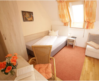 Ein frisch bezogenes Einzelbett in einem lichtgefluteten Raum mit Dachschräge