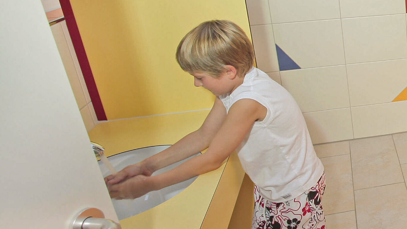 Zwei Kinder in den Kinder-Sanitäranlagen, links ein Waschbecken, rechts kleine Toiletten
