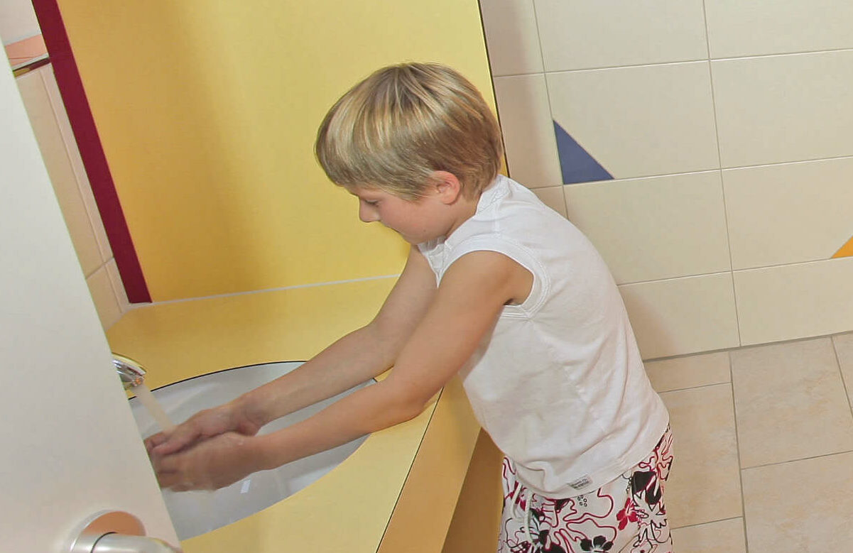 Zwei Kinder in den Kinder-Sanitäranlagen, links ein Waschbecken, rechts kleine Toiletten
