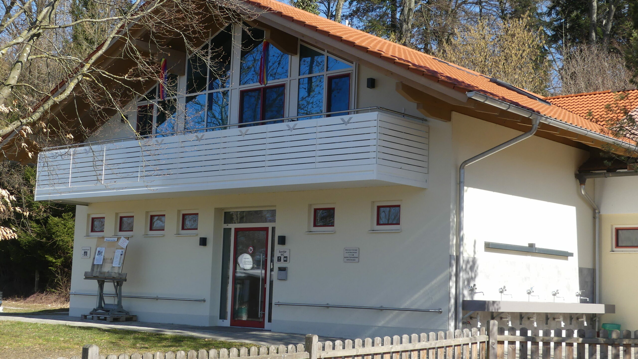 Außenansicht des Sanitär-Gebäudes. Zentral ein großer Eingang mit Glastüre, rechts am Gebäude eine Reihe Waschbecken.