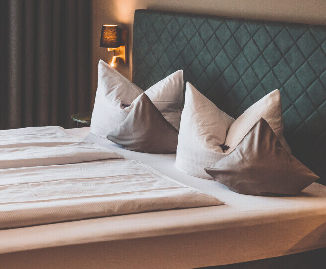 Innenansicht eines frisch hergerichteten Zimmers mit einem Doppelbett und einem Tisch und Sessel