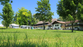 Eine saftig grüne Wiese im Sonnenschein, im Hintergrund das Haupthaus