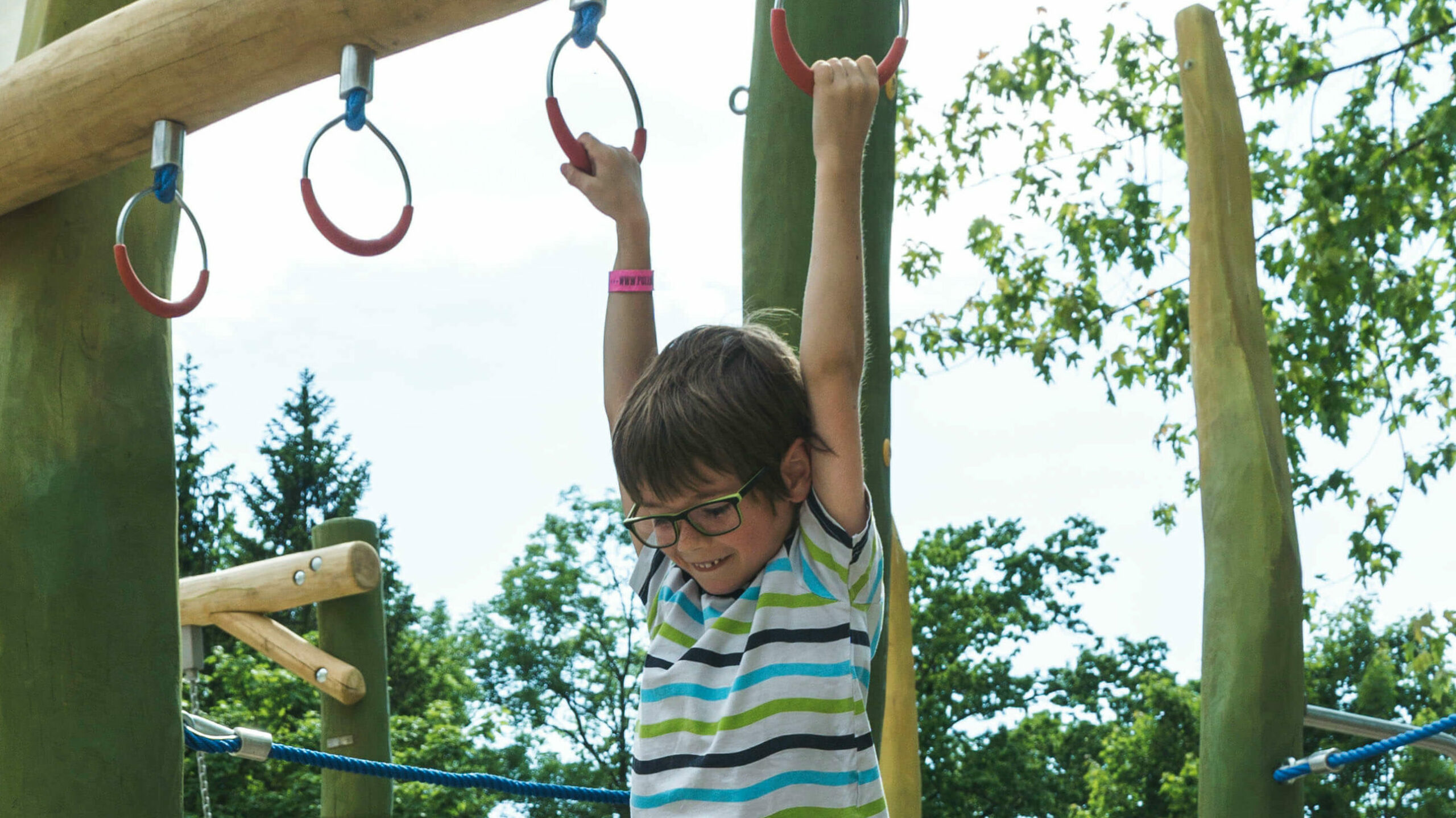Kinder spielen auf einem großen, bunten Klettergerüst. Darunter ist Sand.